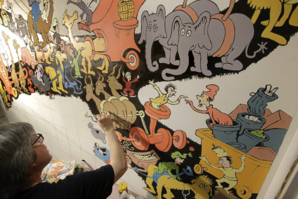 In this May 4, 2017 photo John Simpson, left, project director of exhibitions for The Amazing World of Dr. Seuss Museum, paints a mural based on artwork in the Dr. Seuss book "Did I Ever Tell You How Lucky You Are?" on a wall at the museum, in Springfield, Mass. (AP Photo/Steven Senne)