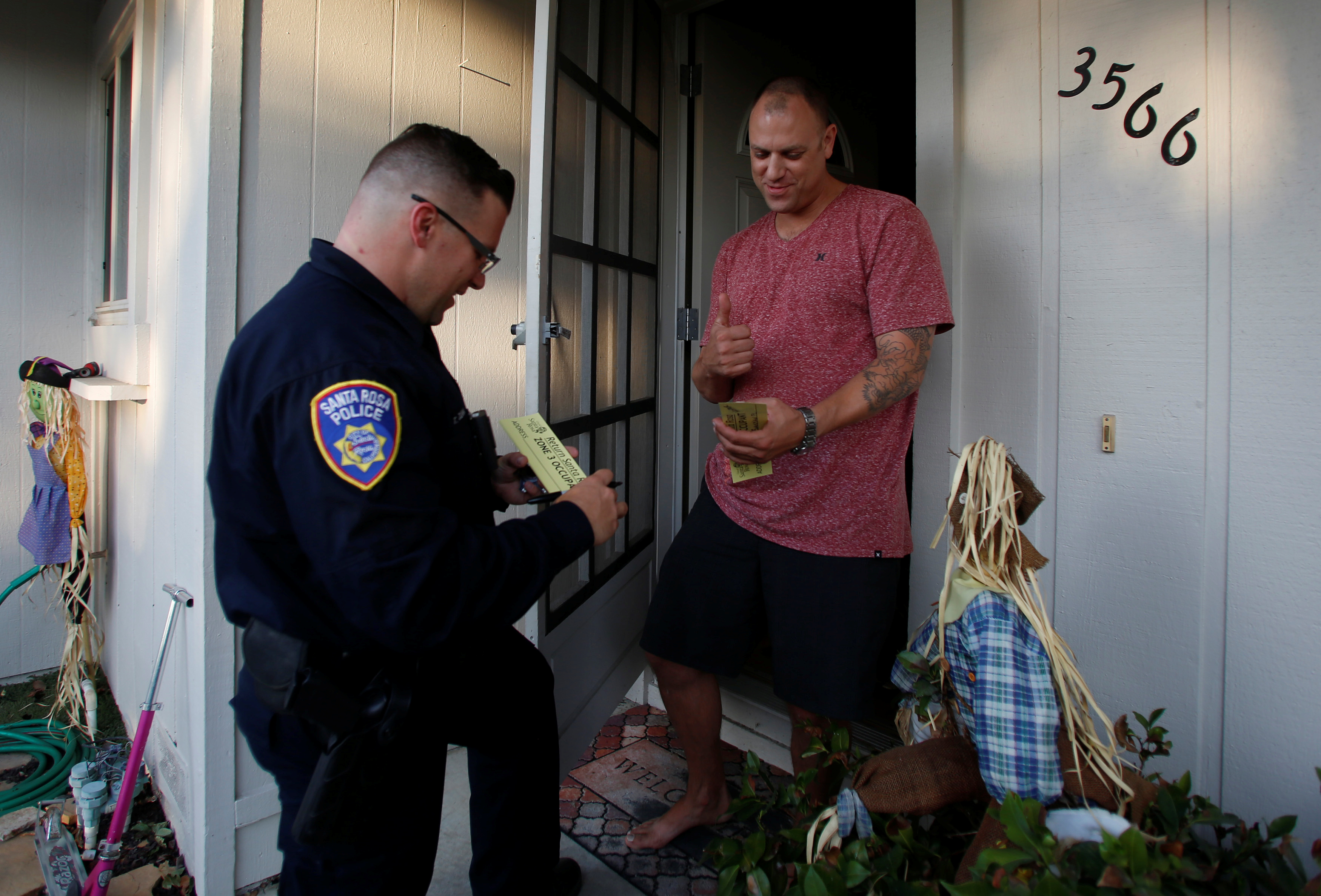 Patrick Seawright (R) reacts as he receives a pass from Santa Rosa police officer Travis Dunn that allows him to come and go from the evacuation zone he lives in after a wildfire tore through adjacent streets in Santa Rosa, Calif., on Oct. 15, 2017. (REUTERS/Jim Urquhart)