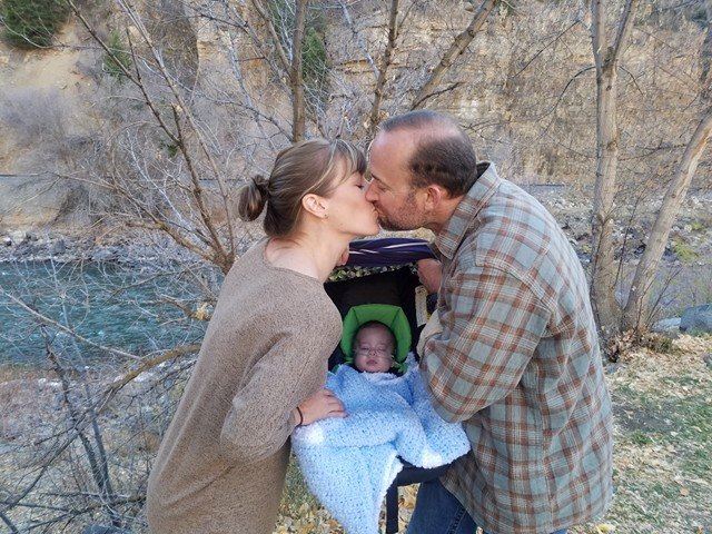 Melissa and Adam Winch kiss over their baby Axel. (Facebook/Adam Winch)