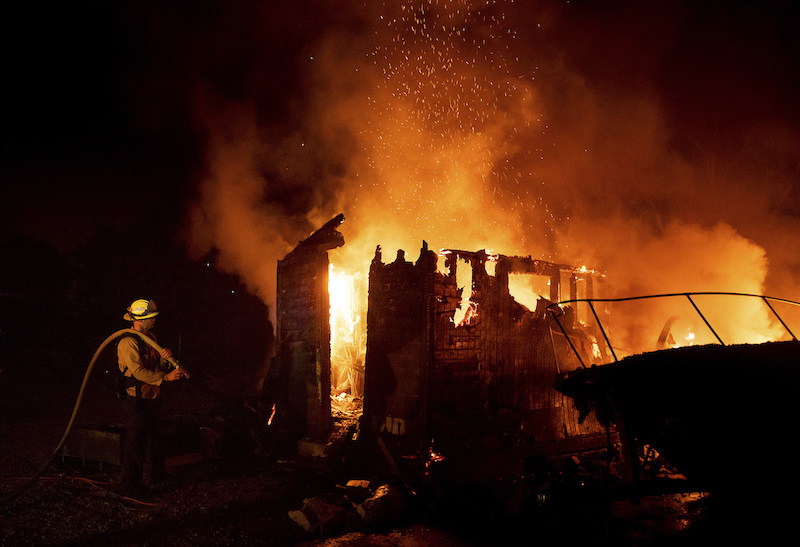 Firefighter Jay Wilkens monitors a flaming shed and boat as the Holiday fire burns in Goleta, Calif., on July 7, 2018. The blaze has destroyed multiple homes. (AP Photo/Noah Berger)