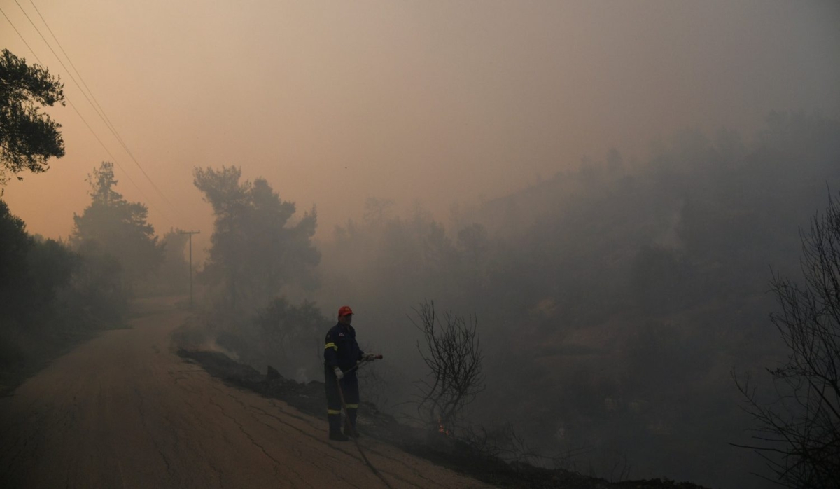 A firefighter throws water through a hose as a wildfire burns near the village of Psahna, in Evia, Greece, Aug. 12, 2018. (Reuters/Michalis Karagiannis)