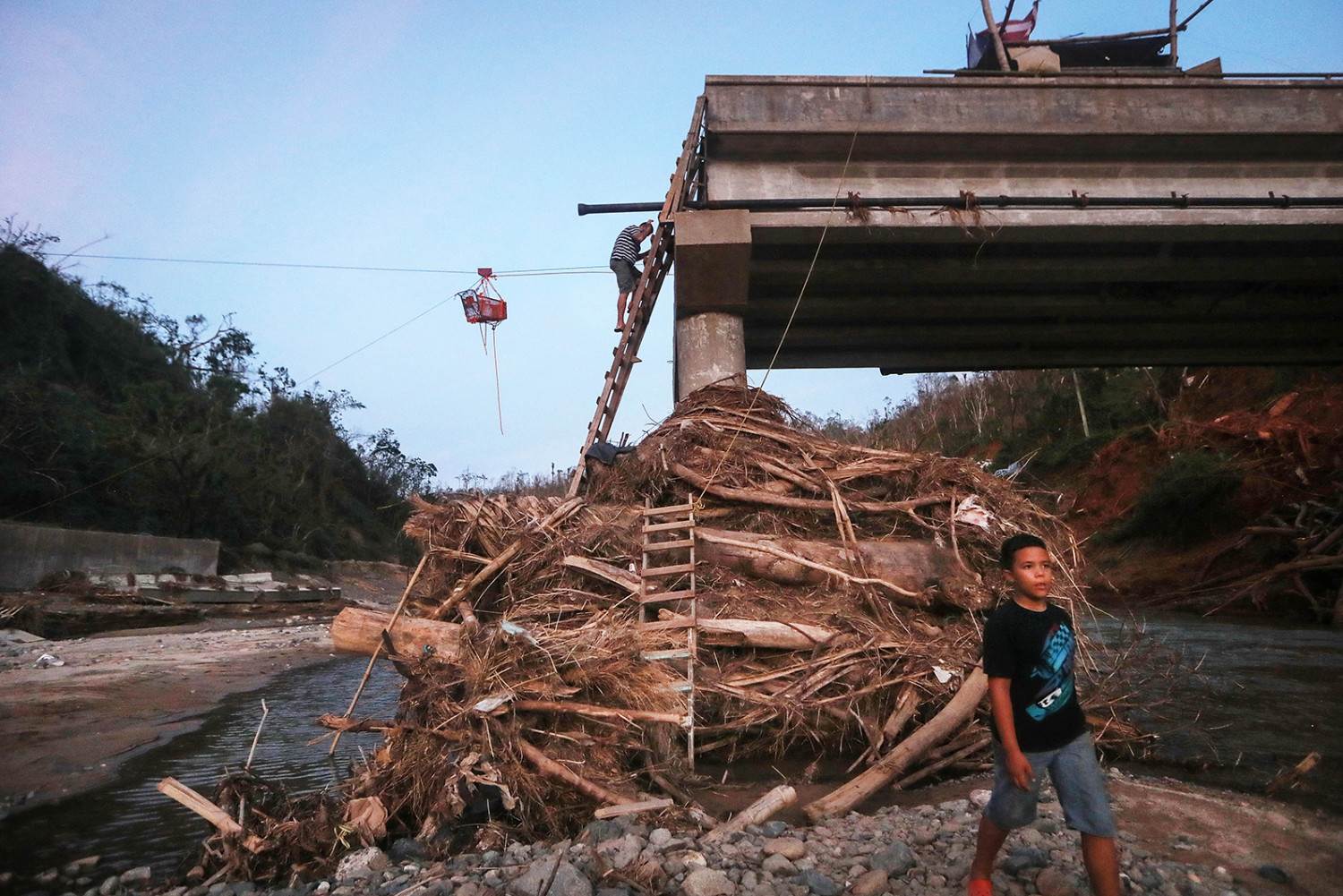 A man descends a makeshift ladder reaching to the top of a broken bridge spanning the Vivi River in Utuado, Puerto Rico on Oct. 20, 2017. (Mario Tama/Getty Images)