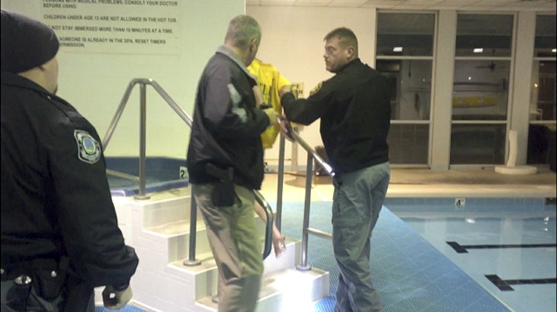 In this photo released by the Pike County Sheriff's Office, Sheriff Charles S. Reader, left, and Interim Waverly Police Chief Dennis Crabtree apprehend an escaped inmate on Tuesday, Dec. 18, 2018, at an Ohio senior living community, in Waverly, Ohio. The inmate is back in custody after being found soaking in a hot tub at the center, still wearing her yellow jail outfit. The Pike County Sheriff's Office says the 34-year-old woman fled while being booked on drug-possession charges Tuesday. (Pike County Sheriff’s Office via AP)