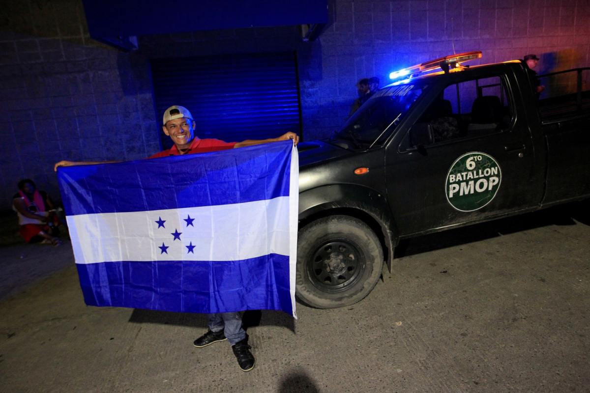 A man holds a flag of Honduras at a bus station in San Pedro Sula in front of a military vehicle before leaving with a new caravan of migrants to the United States, on Jan. 14, 2019. (Jorge Cabrera/Reuters)