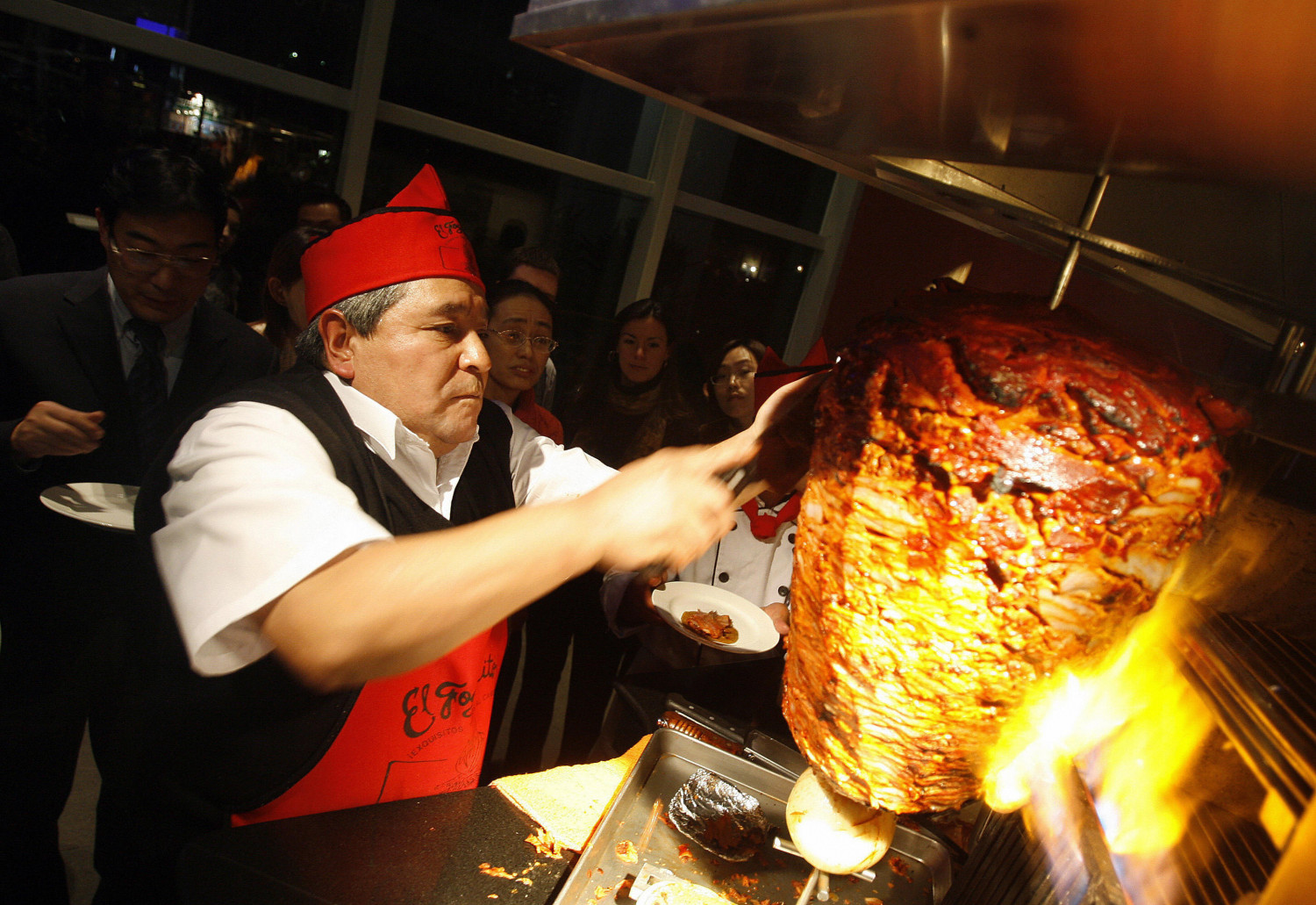 Mexican chef Alberto Juarez Don Beto slices grilled meat onto a hand-held tortilla for a taco al pastor as patrons watch and wait during an opening-event for Mexican restaurant El Fogoncito, 30 January 2007 in Beijing. (Frederic J. Brown/AFP/Getty Images)