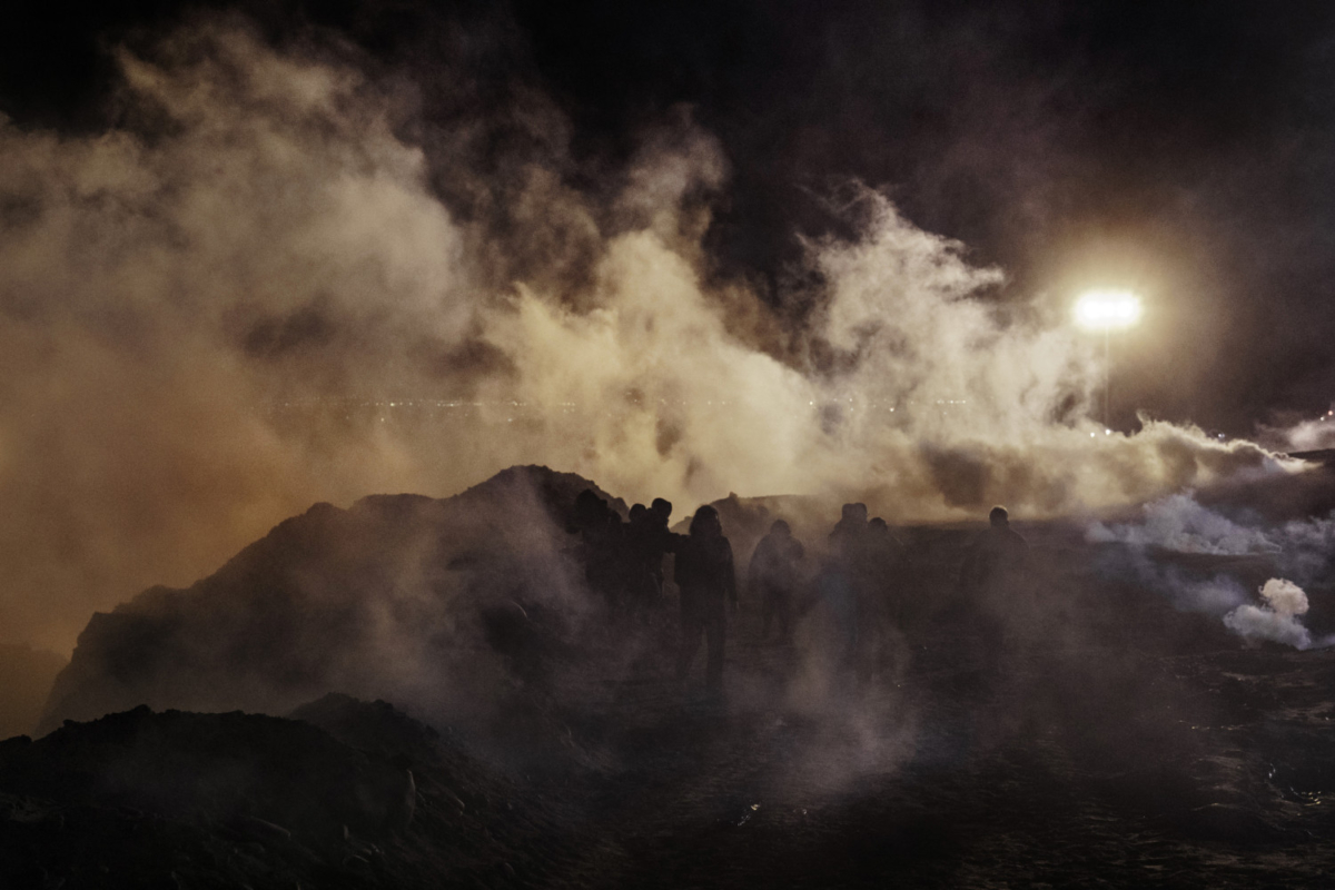 Tear gas thrown by Border Protection officers on the San Diego, Calif. side of the U.S.-Mexico border causes migrants to disperse on the Tijuana, Mexico side of the border on Jan. 1, 2019. (AP Photo/Daniel Ochoa de Olza)