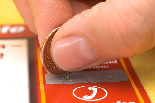 A coin is used to scratch off the metal covering on a lottery ticket. (Shutterstock)