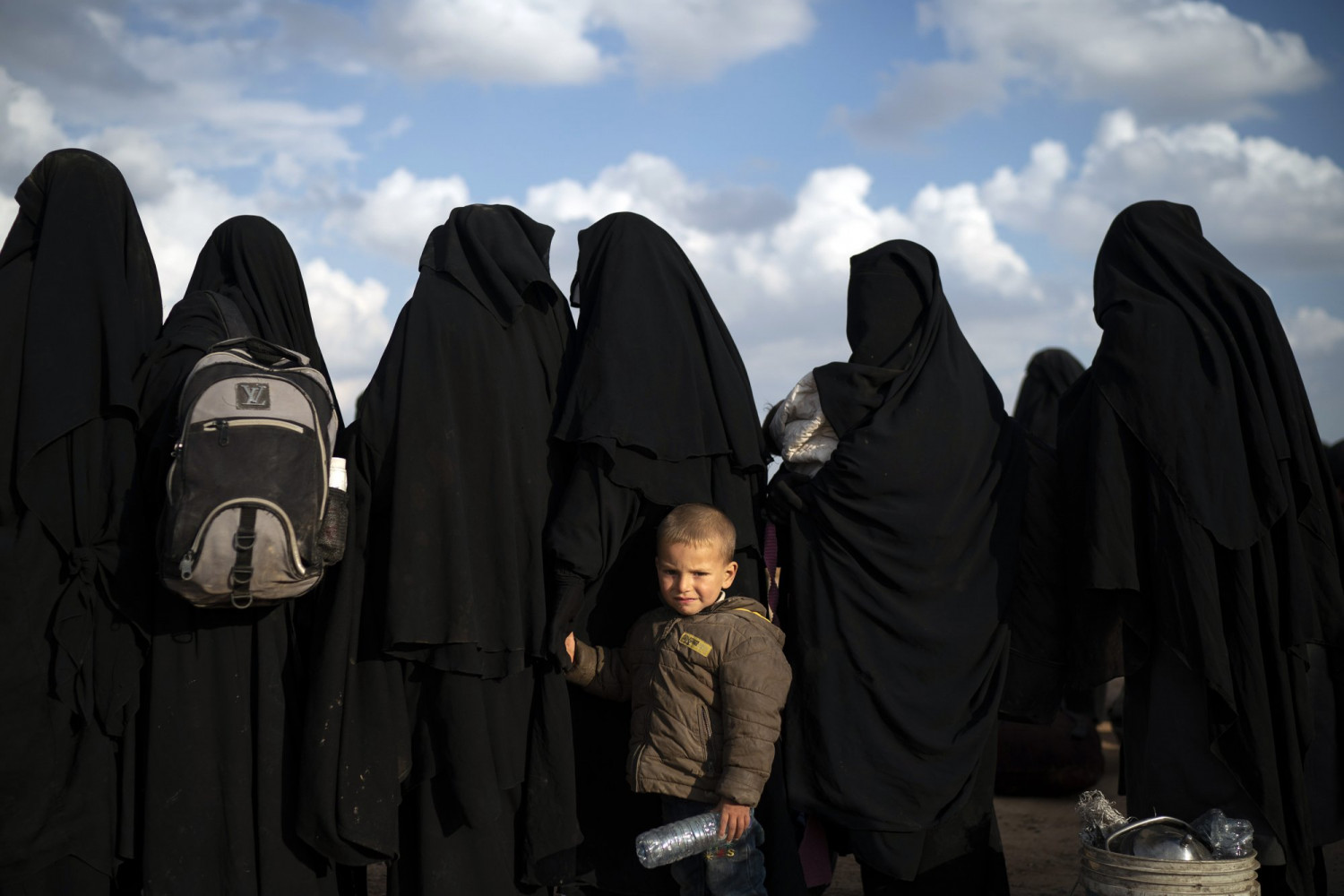 A boy holds her mother's hand as they wait to be screened after being evacuated out of the last territory held by Islamic State militants, near Baghouz, eastern Syria, on Feb. 22, 2019. (Felipe Dana/AP Photo)