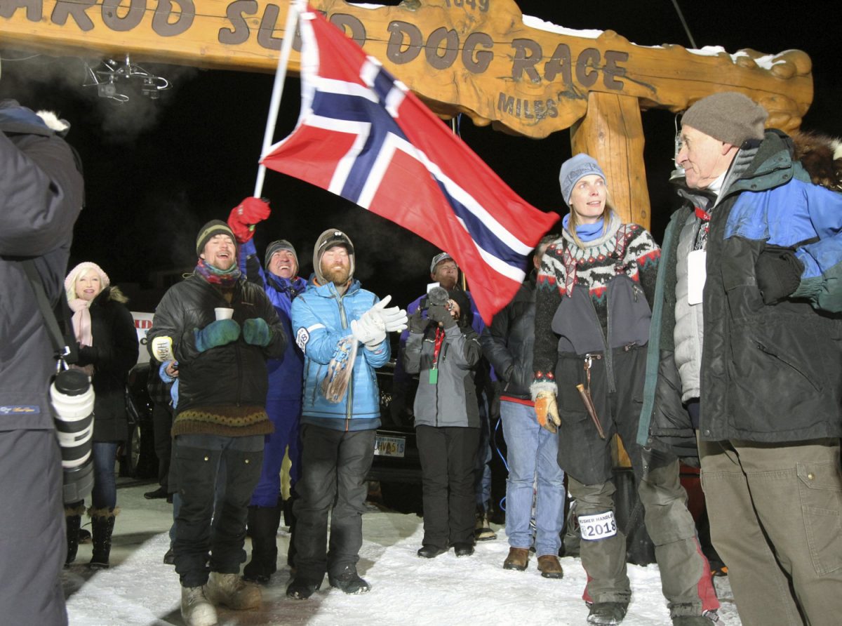 People cheer and wave a Norwegian flag as musher Joar Leifseth Ulsom approaches the finish line to win the Iditarod sled dog race in Nome, Alaska, on March 14, 2018. (Diana Haecker/AP)