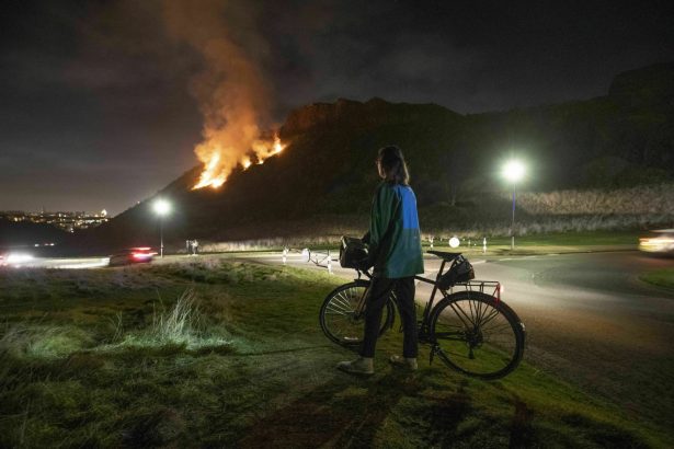 A woman looks at a gorse fire below Salisbury Crags in Holyrood Park, Edinburgh, Scotland, on Feb. 26, 2019. ( Jane Barlow/PA Wire via AP)
