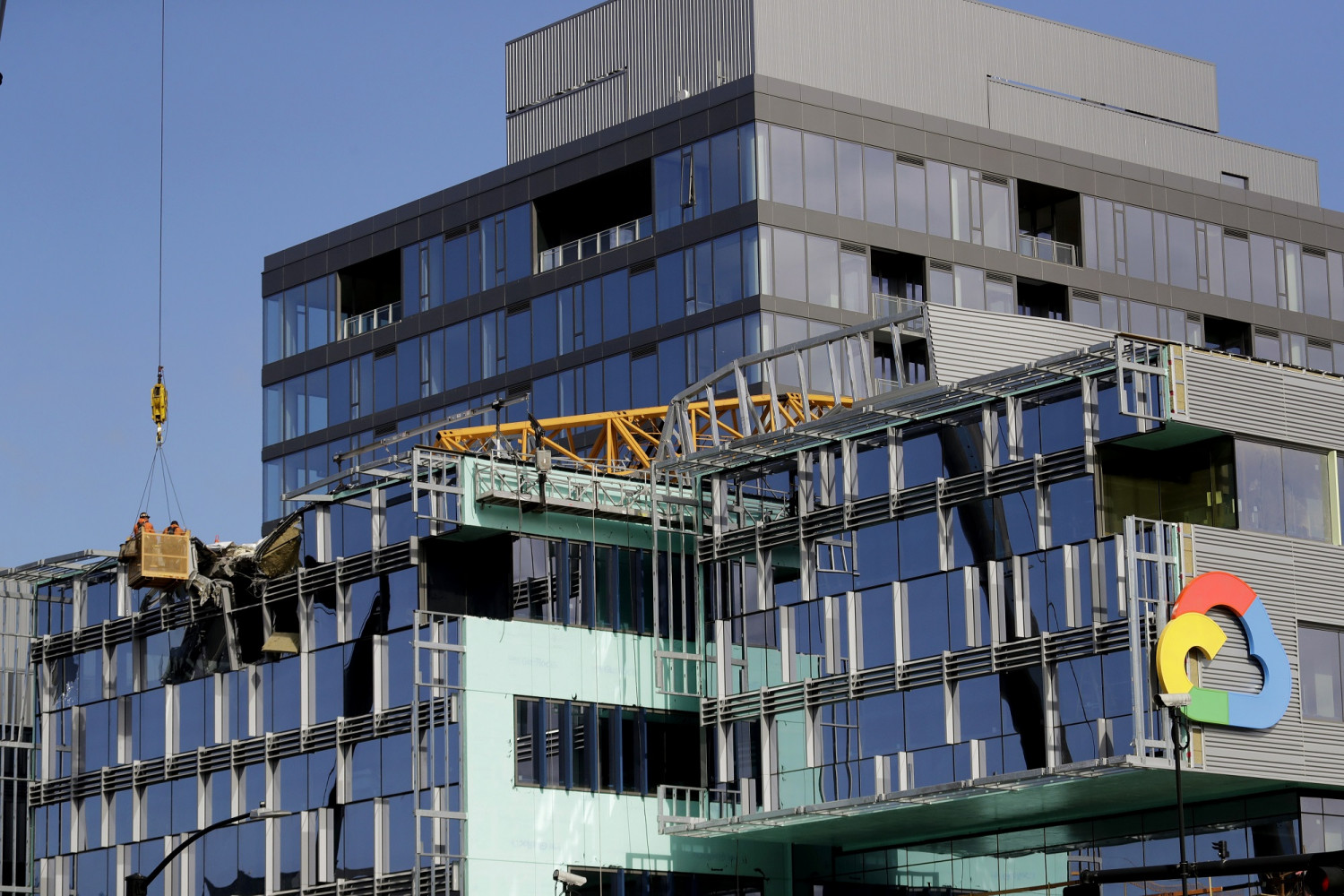With a portion of the broken crane on the roof behind, workers suspended in a basket on April 28, 2019, survey the damage left on the building when the crane atop it collapsed a day earlier in Seattle. (AP Photo/Elaine Thompson)