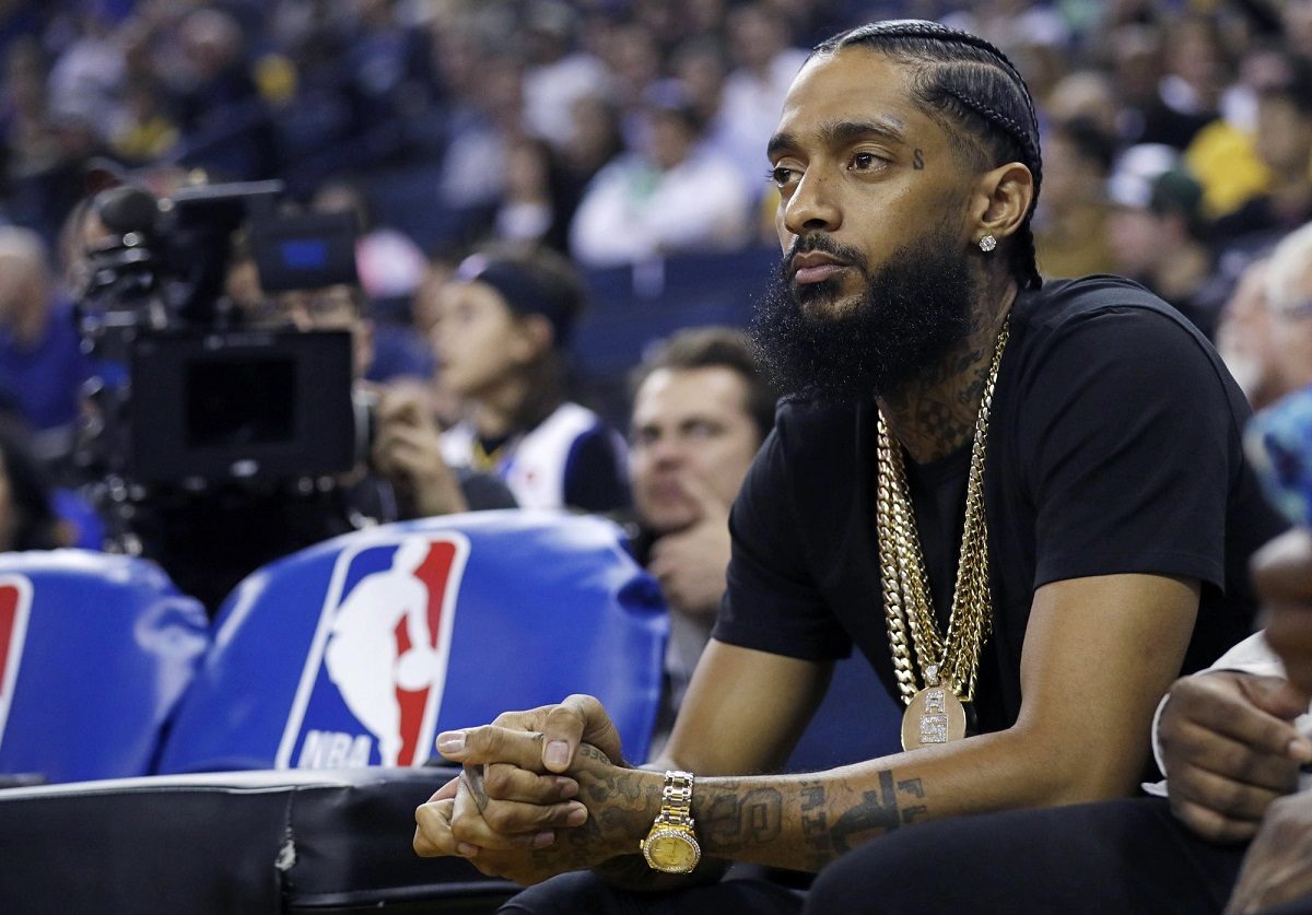 The rapper Nipsey Hussle watches an NBA basketball game between the Golden State Warriors and the Milwaukee Bucks in Oakland, Calif., on March 29, 2018. (AP Photo/Marcio Jose Sanchez, File)