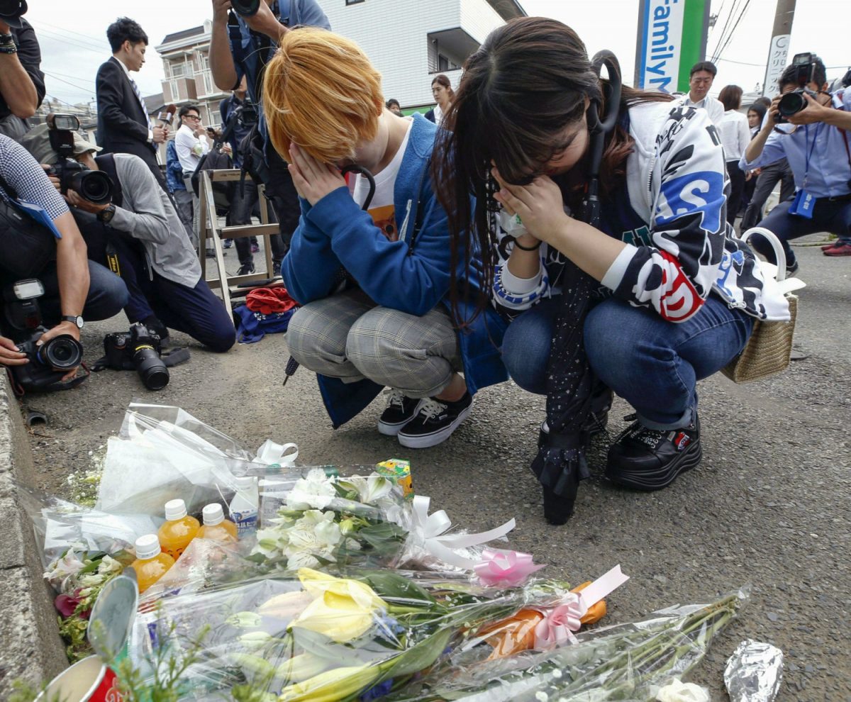 Women pray after offering flowers near the scene where a man wielding a knife attacked commuters in Kawasaki, near Tokyo, Japan on May 28, 2019. (Kyodo News via AP)