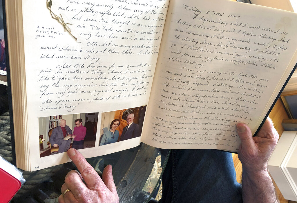 In this June 7, 2019 photo, Ryan Cooper displays pages from a 1973 portion of a diary at his home in Yarmouth, Mass., which he wrote when he visited Otto Frank, the father of the famed Holocaust victim and diarist Anne Frank. Cooper is pointing to a photo of him with Otto Frank while holding Anne's original diary. Cooper has donated a trove of letters and mementos he received from Otto Frank to the U.S. Holocaust Memorial Museum ahead of the 90th anniversary of Anne Frank's birthday. (Philip Marcelo/AP Photo)