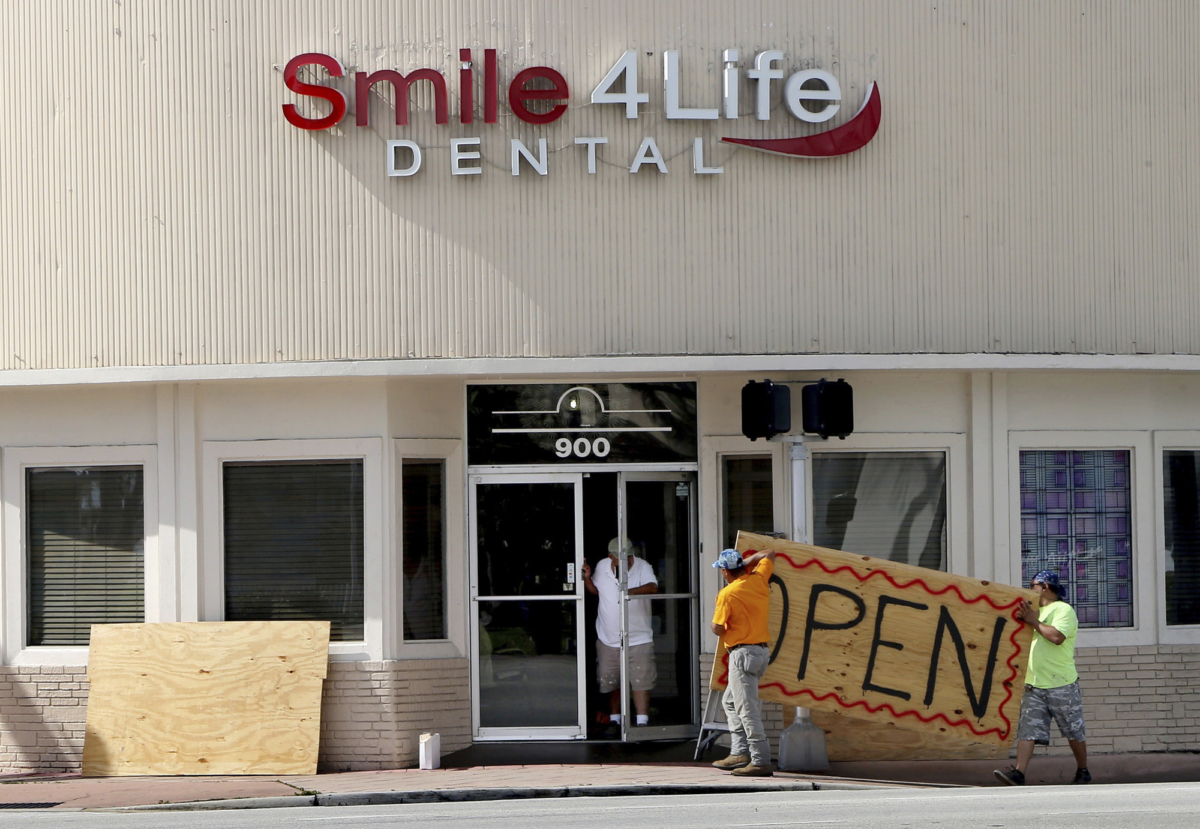 People at a business in the Normandy area in Miami Beach, Fla., remove the plywoods used as shutters covering the front windows on Aug. 31, 2019. (edro Portal/Miami Herald via AP)