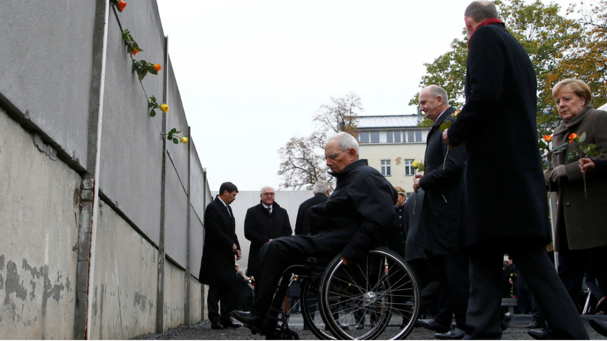 German Chancellor Angela Merkel, Parliament President Wolfgang Schaeuble and Berlin Wall Foundation Director Axel Klausmeier approach the Wall memorial with roses during a ceremony marking the 30th anniversary of the fall of the Berlin Wall at Bernauer Strasse in Berlin, Germany, on Nov. 9, 2019. (Fabrizio Bensch/Reuters)