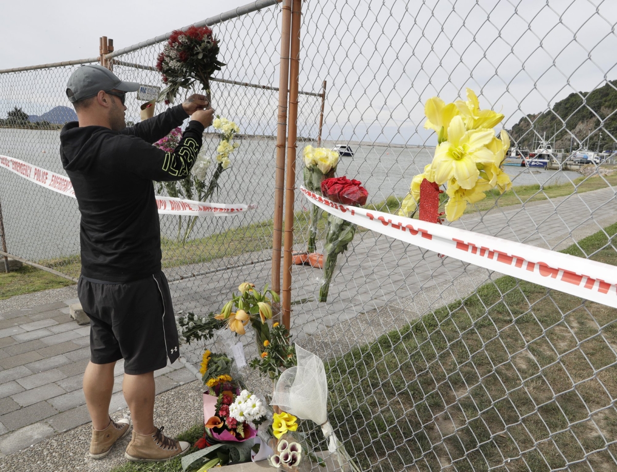 A man places a bouquet to a fence on the waterfront in Whakatane, New Zealand on Dec. 10, 2019. (Mark Baker/AP Photo)
