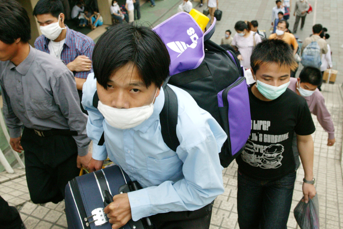 Migrant workers wearing protective face masks make their way to the train station as they leave the city over worries about SARS in Guangzhou, the capital of Guangdong province, China, on May 2, 2003. (Christian Keenan/Getty Images)
