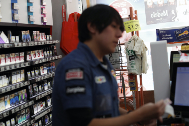 Reusable red shopping bags and biodegradable, compostable bags are displayed for purchase by customers needing bags, as a cashier makes change at a Circle K convenience store in Mexico City, on Wednesday, Jan. 1, 2020. (Rebecca Blackwell/AP)