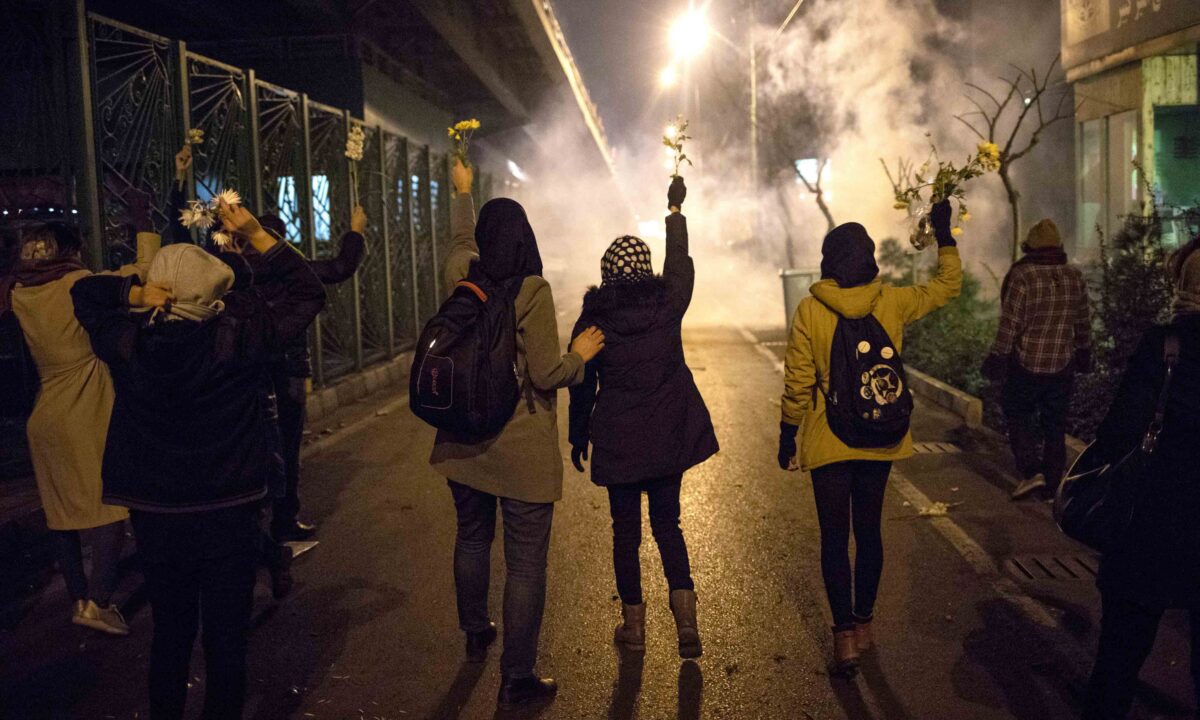 Protesters hold flowers as tear gas fired by police rises at a demonstration in front of Amir Kabir University to remember victims of a Ukrainian airplane shot down by an Iranian missile, in Tehran, Iran, on Jan. 11, 2020. (AP Photo)