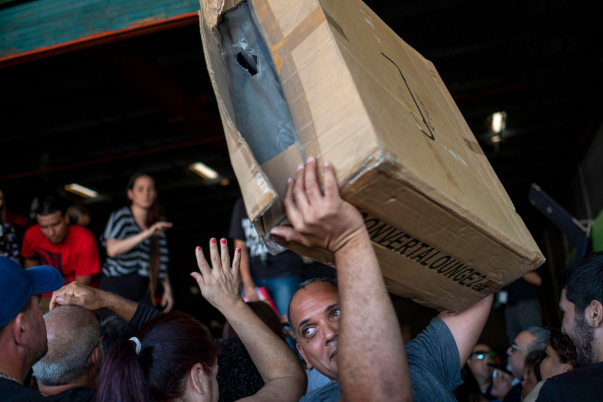 People carry supplies after breaking into a warehouse with supplies believed to have been from when Hurricane Maria struck the island in 2017, in Ponce, Puerto Rico, on Jan. 18, 2020. (Ricardo Arduengo/AFP via Getty Images)