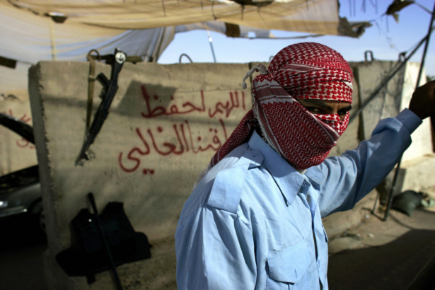 Wearing a traditional headscarf to protect his identity from pedestrians, an Iraqi policeman checks a car at an entry control point into the restive city of Fallujah, Iraq, on Nov. 14, 2006. (David Furst/AFP via Getty Images)
