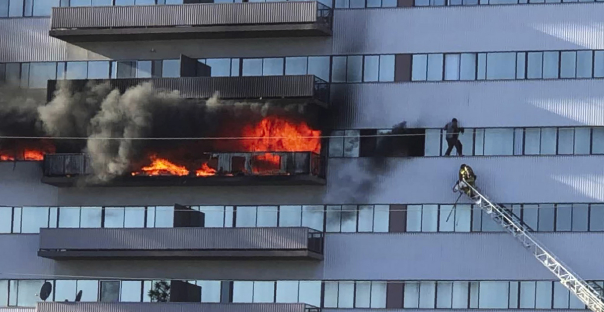 This image from video by Jenna Fabian shows a Los Angeles Fire Department firefighter on a ladder rescuing a man who had climbed out on the side of a 25-story high-rise apartment, escaping flames from a burning apartment balcony, after a fire broke out on a sixth-floor balcony and sent choking smoke billowing through the upper levels in West Los Angeles on Jan. 29, 2020. (Courtesy of Jenna Fabian via AP)