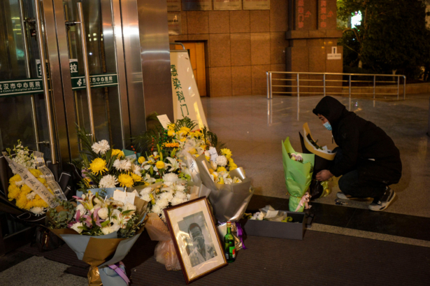 A man placing flowers beside a photo of the late ophthalmologist Li Wenliang outside the Houhu Branch of Wuhan Central Hospital in Wuhan in China's central Hubei province, on Feb. 7, 2020.(STR/AFP via Getty Images)