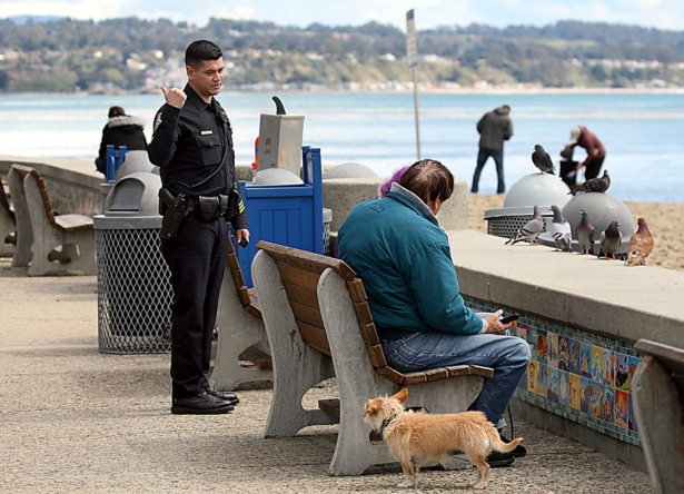 Police Sgt. Leo Moreno tells a couple they have to keep moving and can't sit on the Esplanade bench in Capitola, Calif., on March 25, 2020. (Dan Coyro/The Santa Cruz Sentinel via AP)