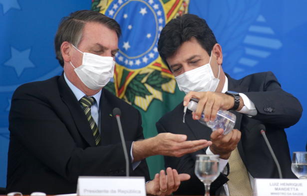 Brazilian Health Minister Luiz Henrique Mandetta (D) gives gel alcohol to President Jair Bolsonaro, both using protective masks, during a press conference about government plans and measures about the COVID-19 disease outbreak in Brazil, at the Planalto Palace in Brasilia, Brazil on March 18, 2020. (Andre Coelho/Getty Images)
