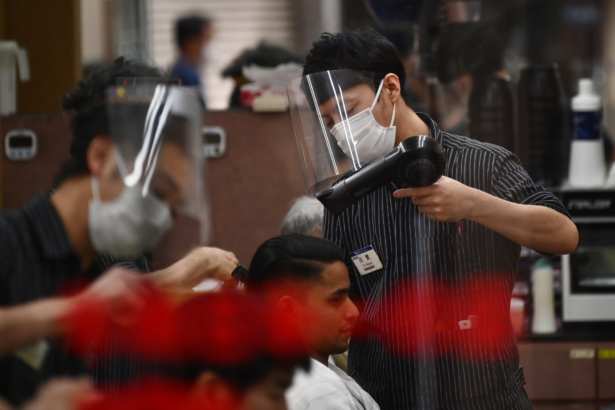 Employees wearing masks and shields amid the CCP virus pandemic style customers' hair at a hair salon in Tokyo on April 28, 2020. (Charly Triballeau/ AFP via Getty Images)