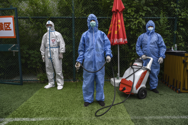 Chinese epidemic control workers wear protective suits as they disinfect an area where people were lining up for a nucleic acid swab test for COVID-19 at a government testing site in Xicheng District during an organized tour in Beijing, China, on June 24, 2020. (Kevin Frayer/Getty Images)
