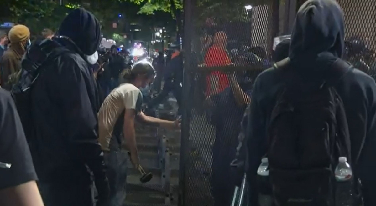 In this still image from video, rioters remove fencing with a construction hammer and other tools in Portland, Ore., on July 18, 2020. (CNN)