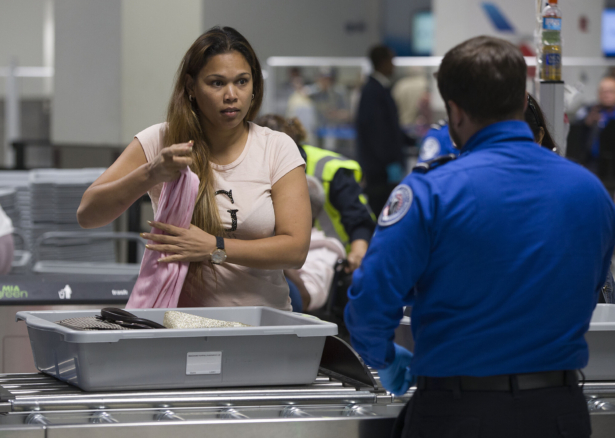 A traveler places her carry on items into a tray as a Transportation Security Administration (TSA) agent helps her use the 3D scanner at Miami International Airport on May 21, 2019. (Joe Raedle/Getty Images)