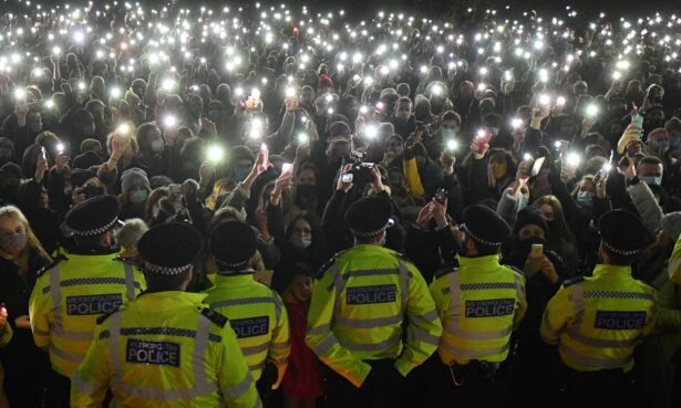 Police officers form a cordon as a crowd turn on their phone torches at a band-stand where a planned vigil in honour of Sarah Everard was cancelled due to coronavirus restrictions, on Clapham Common, south London, UK, on March 13, 2021. (Justin Tallis/AFP via Getty Images)