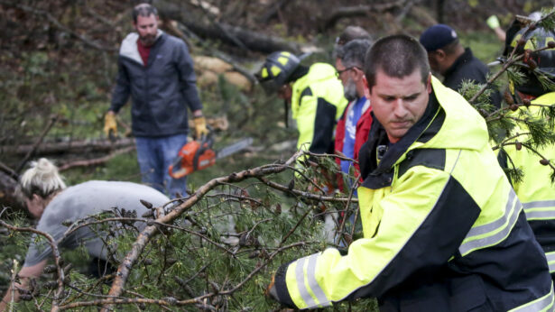 A firefighter works with residents to remove fallen trees