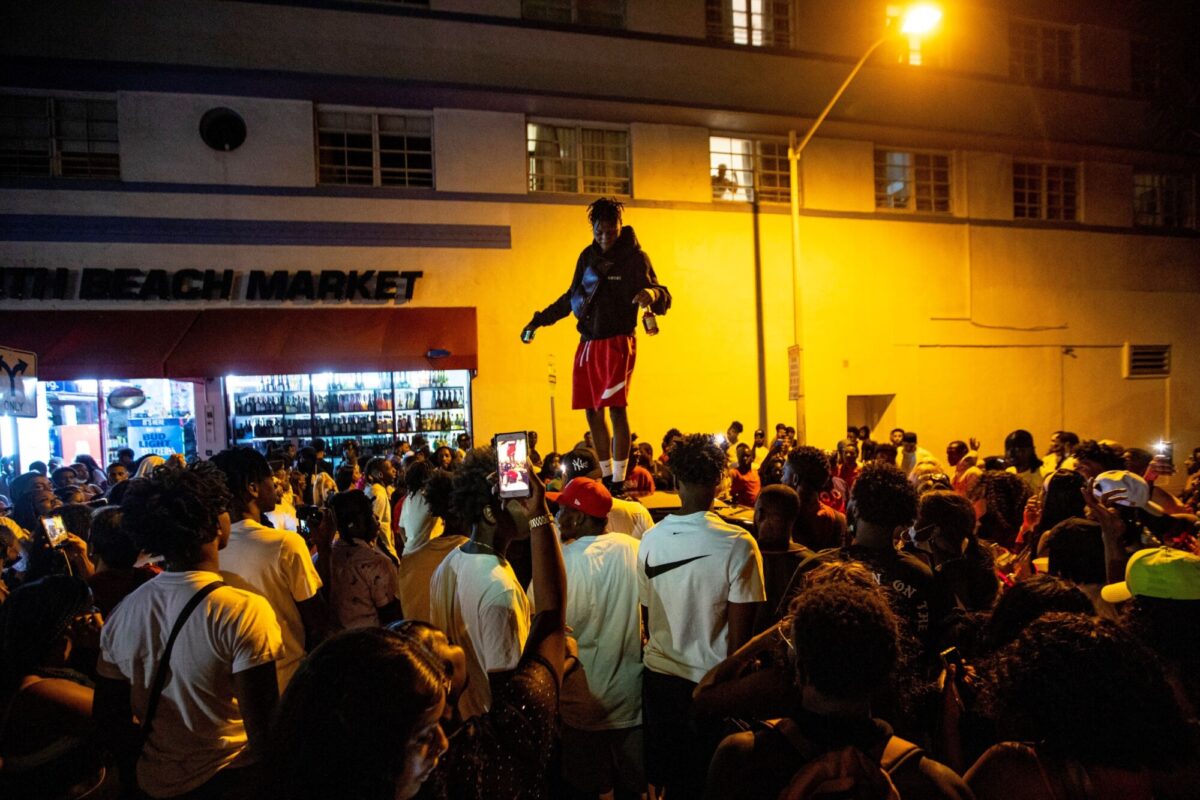 A man stands on a car as crowds defiantly gather in the street while a speaker blasts music an hour past curfew in Miami Beach, Fla., on March 21, 2021. (Daniel A. Varela/Miami Herald via AP)