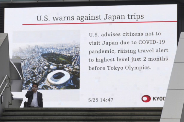A man walks in front of a screen showing the news on U.S. warning against visits to Japan, in Tokyo, on May 25, 2021. (Eugene Hoshiko/AP Photo)