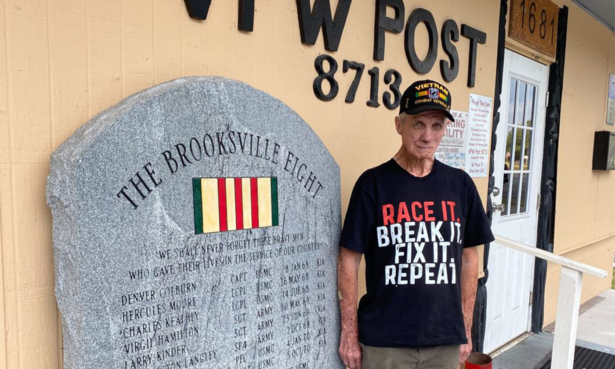 Ron McCombs, retired United States Army, stands at attention beside The Brooksville Eight monument at VFW Post 8713 in Brooksville, Florida. (Patricia Tolson/The Epoch Times)