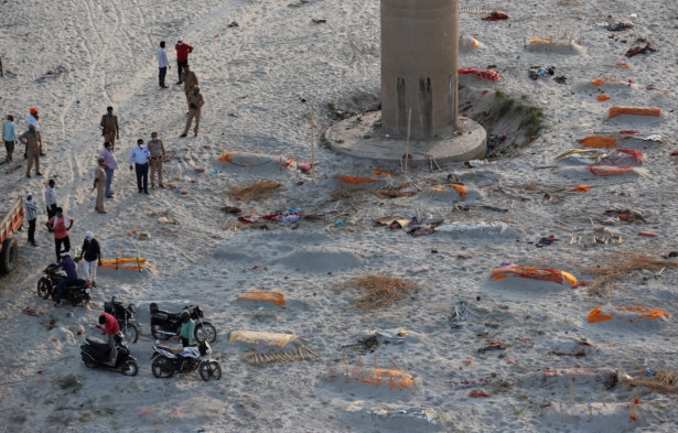 Policemen stand next to the bodies buried in shallow graves on the banks of Ganges river in Prayagraj, India, on May 15, 2021. (Rajesh Kumar Singh/AP Photo)