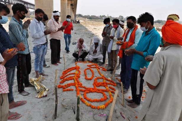Family members and relatives of a person who died pray next to his shallow sand grave on the banks of river Ganges in Prayagraj, India, on May 16, 2021. (Rajesh Kumar Singh/AP Photo)