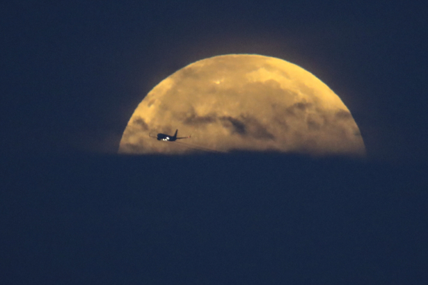 An airplane flies past as the full-moon sets over Santa Monica Beach in Santa Monica, Calif., on May 26, 2021. (Ringo H.W. Chiu/AP Photo)