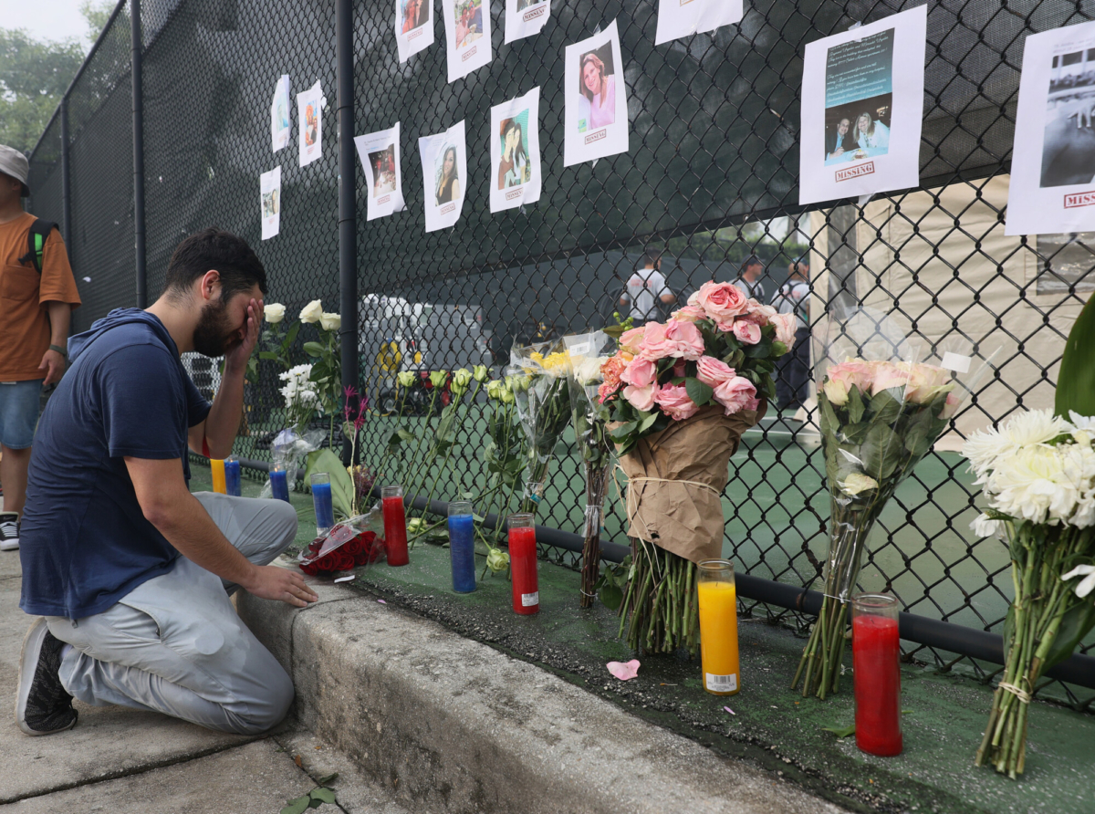 Leo Soto kneels in front of a memorial that includes pictures of missing people in Surfside, Fla., on June 25, 2021. (Joe Raedle/Getty Images)