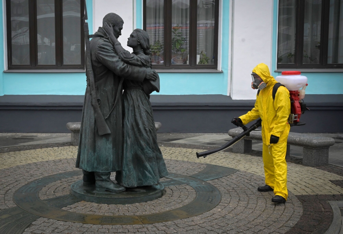 A serviceman of the Russian Ministry for Civil Defence, Emergencies, and Elimination of Consequences of Natural Disasters, wearing protective gear, disinfects Moscow's Belorussky railway station next to a statue, amid the COVID-19 pandemic, Russia, on June 11, 2021. (Natalia Kolesnikova/AFP via Getty Images)
