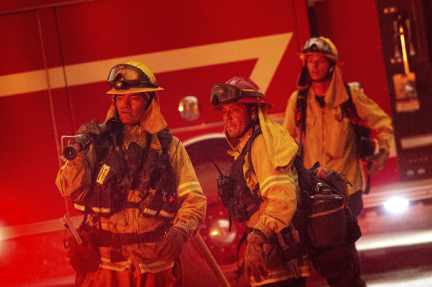 Firefighters watch flames burst from a propane tank