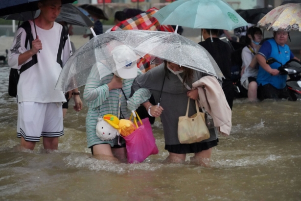 Residents, holding umbrellas amid heavy rainfall, wade through floodwaters on a road in Zhengzhou, Henan province, China, on July 20, 2021. (cnsphoto via Reuters)