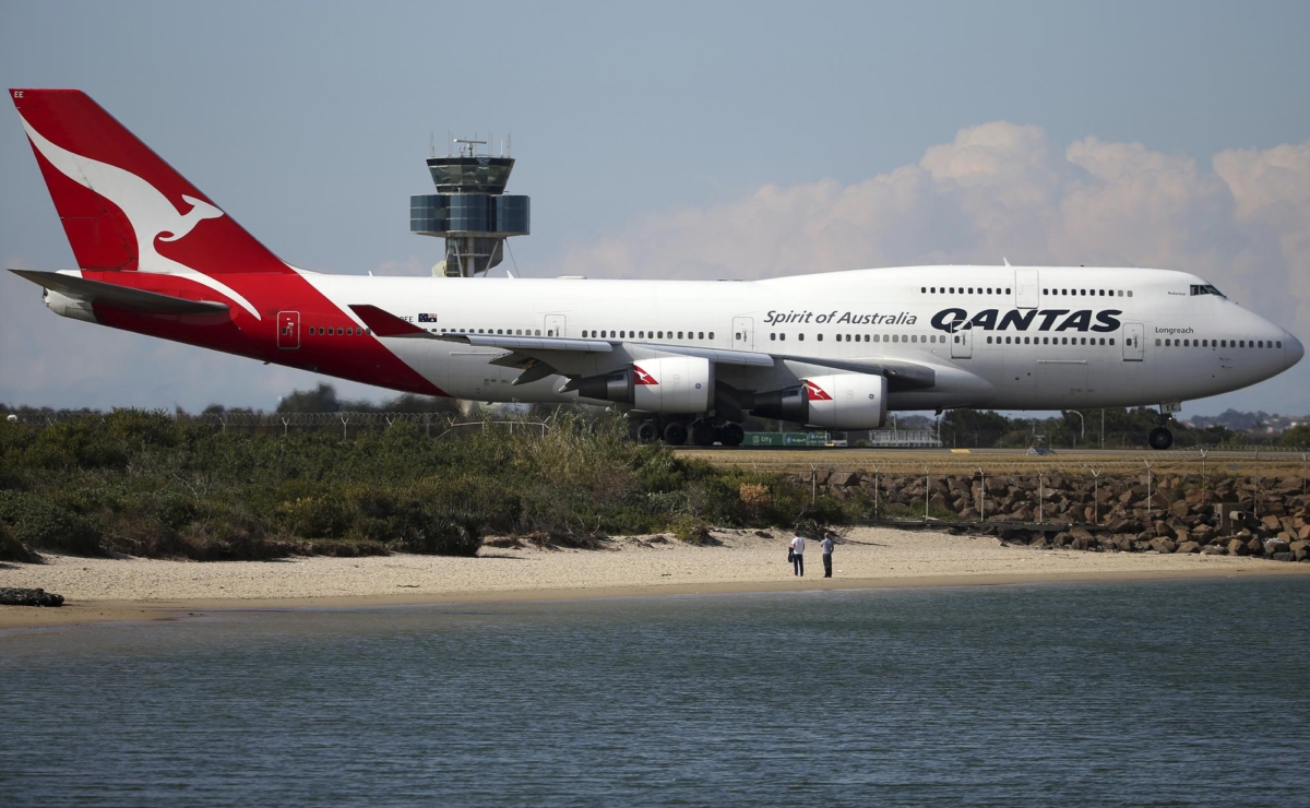 Two people watch from a beach as a Qantas plane taxies on the runway at Sydney Airport in Sydney, Australia, on Aug. 20, 2015. (Rick Rycroft/AP Photo)