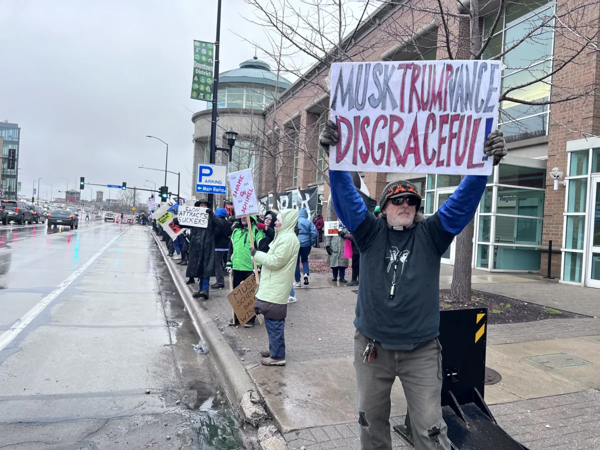 A man displays a protest sign outside a town hall meeting hosted by Elon Musk in Green Bay, Wis., on March 30, 2025. (Lawrence Wilson/The Epoch Times)