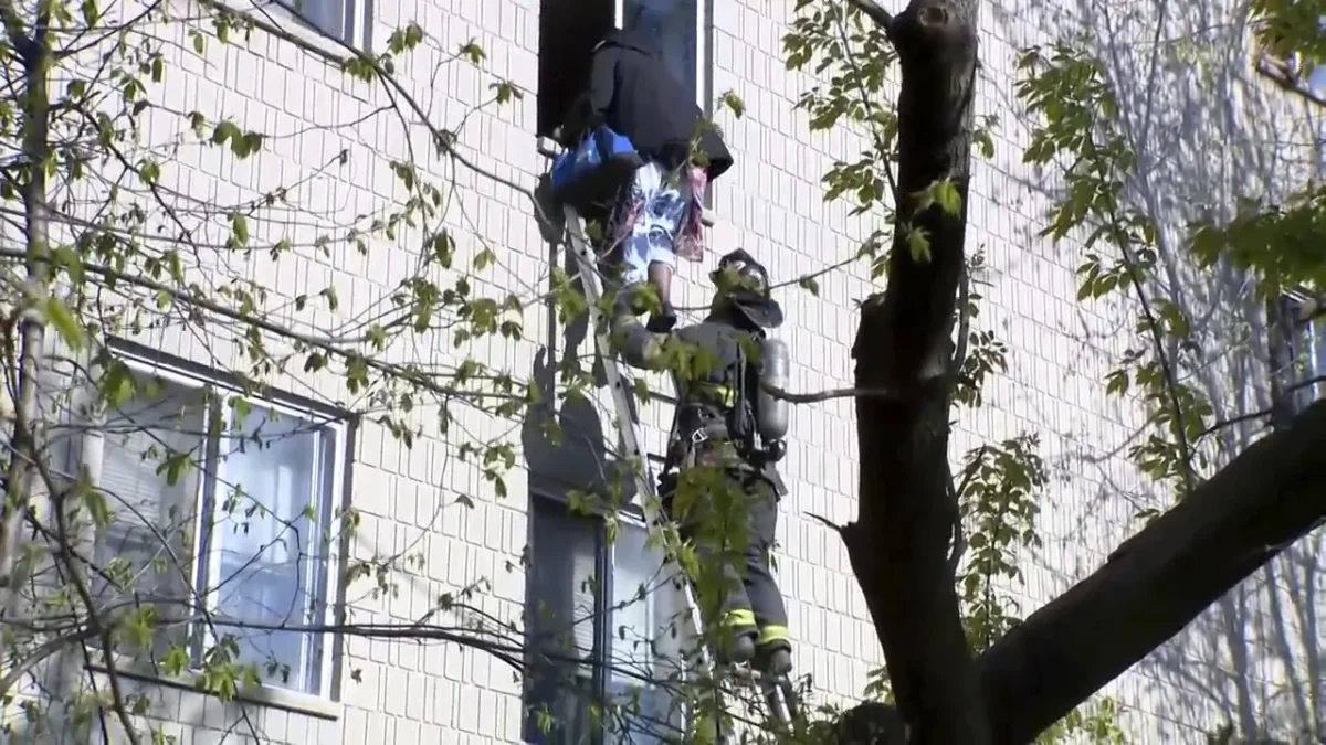 A firefighter on ladder helps a person out of the window at the site of an apartment building fire in Milwaukee, Wisconsin, on May 11, 2025, in a still from video. (WISN via AP)