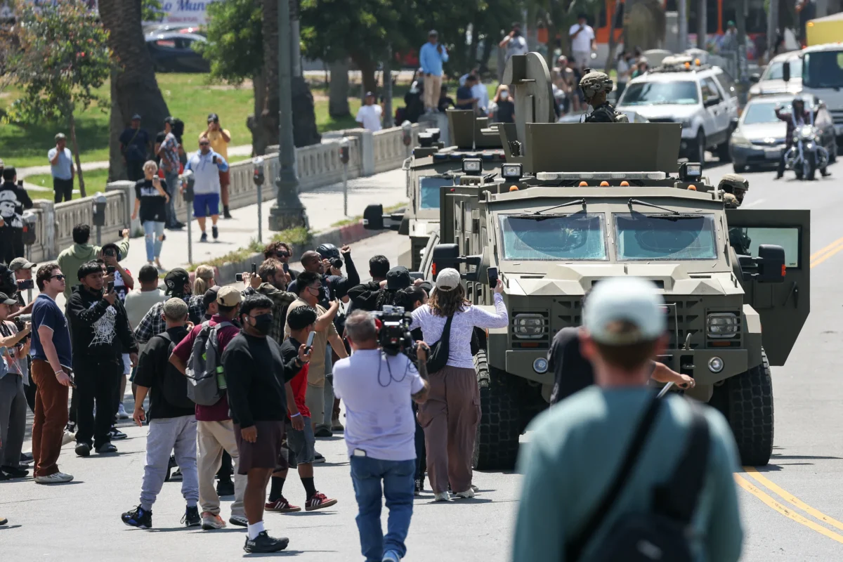 Crowds watch as federal agents with US Customs and Border Patrol (CBP) ride on an armored vehicle driving slowly down Whilshire Boulevard near MacArthur Park in Los Angeles, on July 7, 2025. (Patrick T. Fallon/AFP via Getty Images)